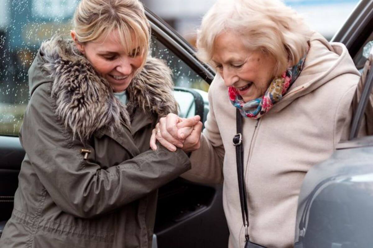 Alltagsbegleiterin hilft einer Seniorin beim Aussteigen aus dem Auto.