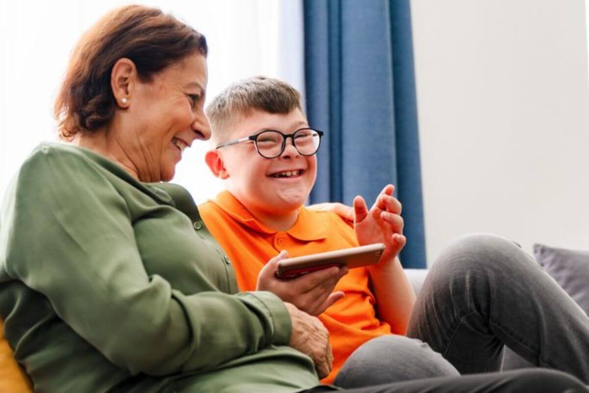 Frau und Kind sitzen gemeinsam auf dem Sofa, lächeln und beschäftigen sich mit einem Tablet.
