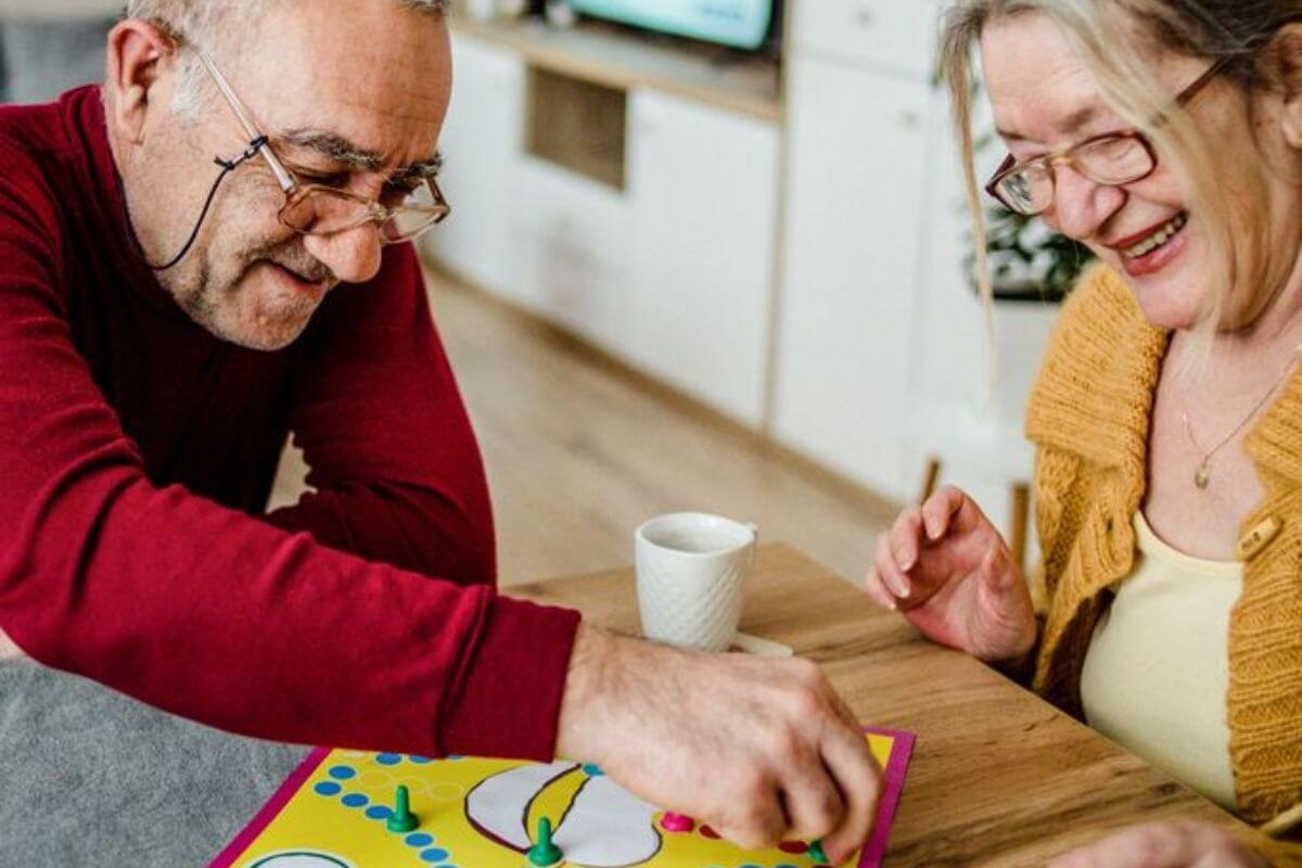 Zwei Senioren spielen gemeinsam ein Brettspiel am Tisch und lachen.